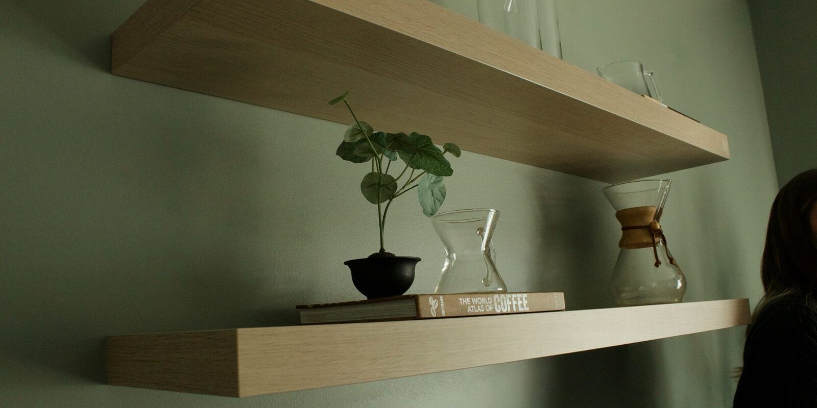 Houten zwevende planken met boeken, planten en glazen karaffen tegen een groen geverfde muur