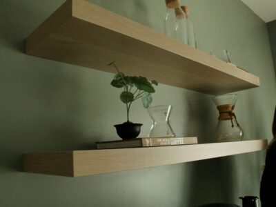 Houten zwevende planken met boeken, planten en glazen karaffen tegen een groen geverfde muur