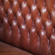 Close-up van een bruine leren bank met capitonnage, waarop je de structuur van het leer goed ziet
